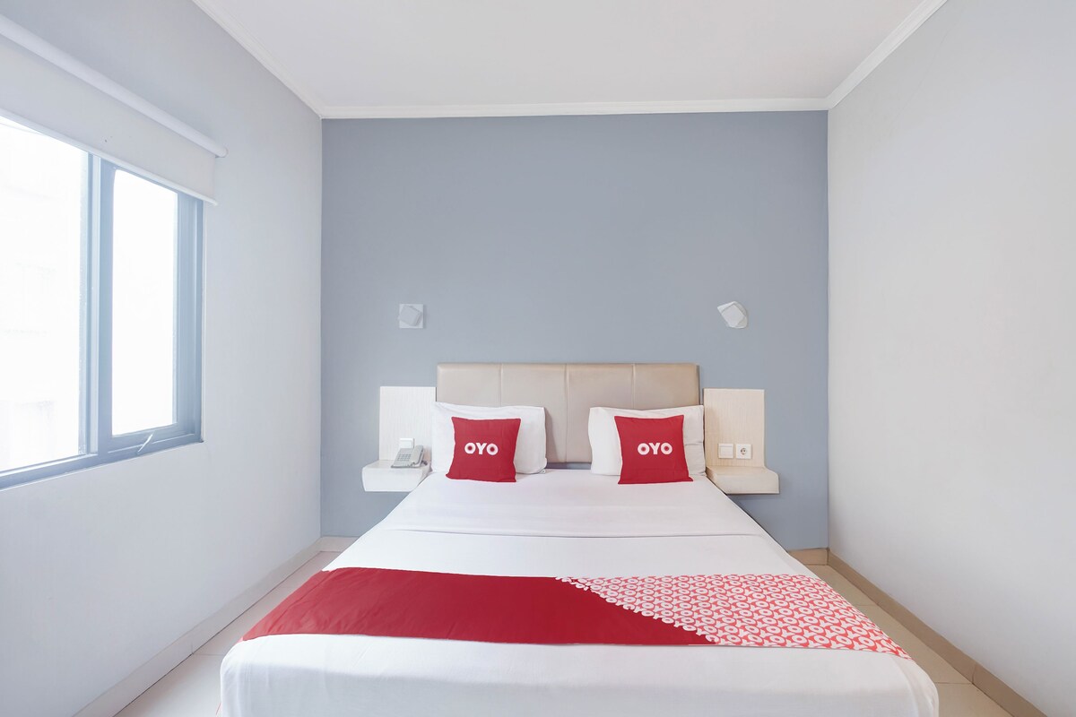 A hotel room with a bed, two pillows, a nightstand, a phone, and a window.