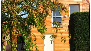 A modern two-story building with a wooden facade, a white door, and a window.