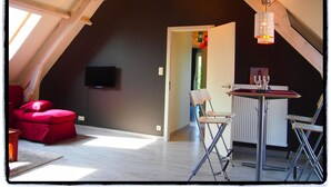 An attic room with a red sofa, a dining table with chairs, a TV, and a window.