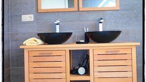 A bathroom with two black vessel sinks, wooden cabinets with drawers, a mirror above the sinks, and a small clock on the cabinet.