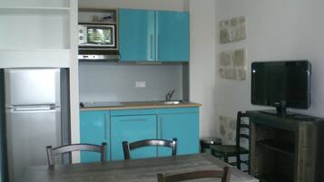 Eine kompakte Küche mit Mikrowelle, Spüle und Schränken. Ein Esstisch mit Stühlen und ein Fernseher auf einem Schrank.
