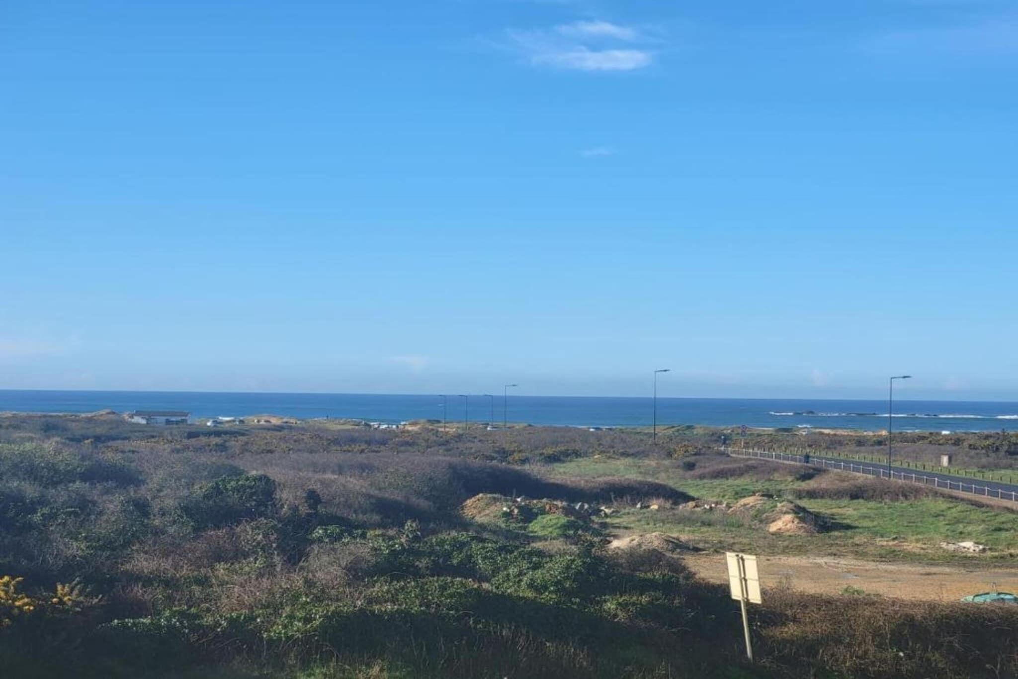 Eine Küstenlandschaft mit blauem Himmel, einer Straße und Gebäuden in der Ferne.