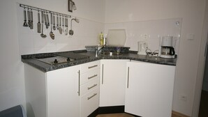 Una cocina compacta con armarios blancos, encimera de granito, cafetera y un colgador para utensilios.