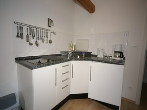 A compact kitchen with white cabinets, a granite countertop, a coffee maker, and a hanging utensil rack.