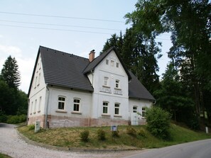 A two-story building with a gabled roof, a stone foundation, and a sign indicating it is a hotel.