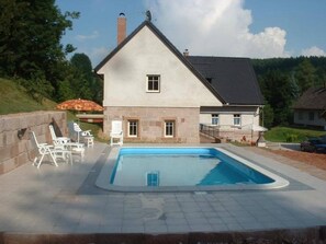 Ett tvåvåningshus med en swimmingpool, en fasad av sten och en liten uteplats med stolar.