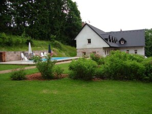A house with a swimming pool, surrounded by greenery and a hillside.