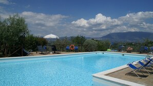 Una piscina con sillas de descanso y sombrillas, rodeada de árboles y montañas al fondo.