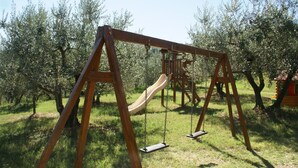Un conjunto de columpios de madera con un tobogán en un área verde rodeada de árboles.