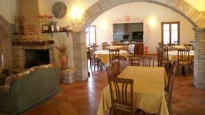 Un comedor con mesas y sillas, una chimenea y una cocina al fondo.