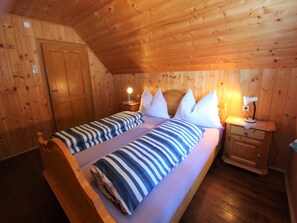 Cozy cabin retreat with a sloped ceiling, featuring a comfortable bed and wooden wardrobe.