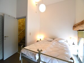 A bedroom with a bed, bedside lamps, a door, and a staircase. - Stylish Duplex with Sauna (Clavier Station)