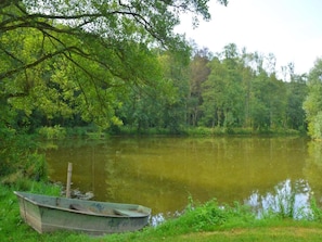 A calm lake with a small boat docked on the grassy shore, surrounded by dense green foliage.