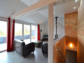 A modern living area with a sofa, a coffee table, and a TV. There is a staircase with a railing leading to an upper level. - Stylish Duplex with Sauna (Clavier Station)