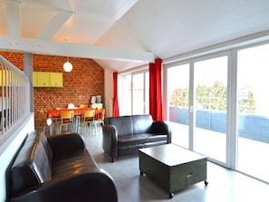 Un salon moderne avec un mur en briques, un coin repas avec une table et des chaises, et une grande porte-fenêtre coulissante donnant sur un espace extérieur.