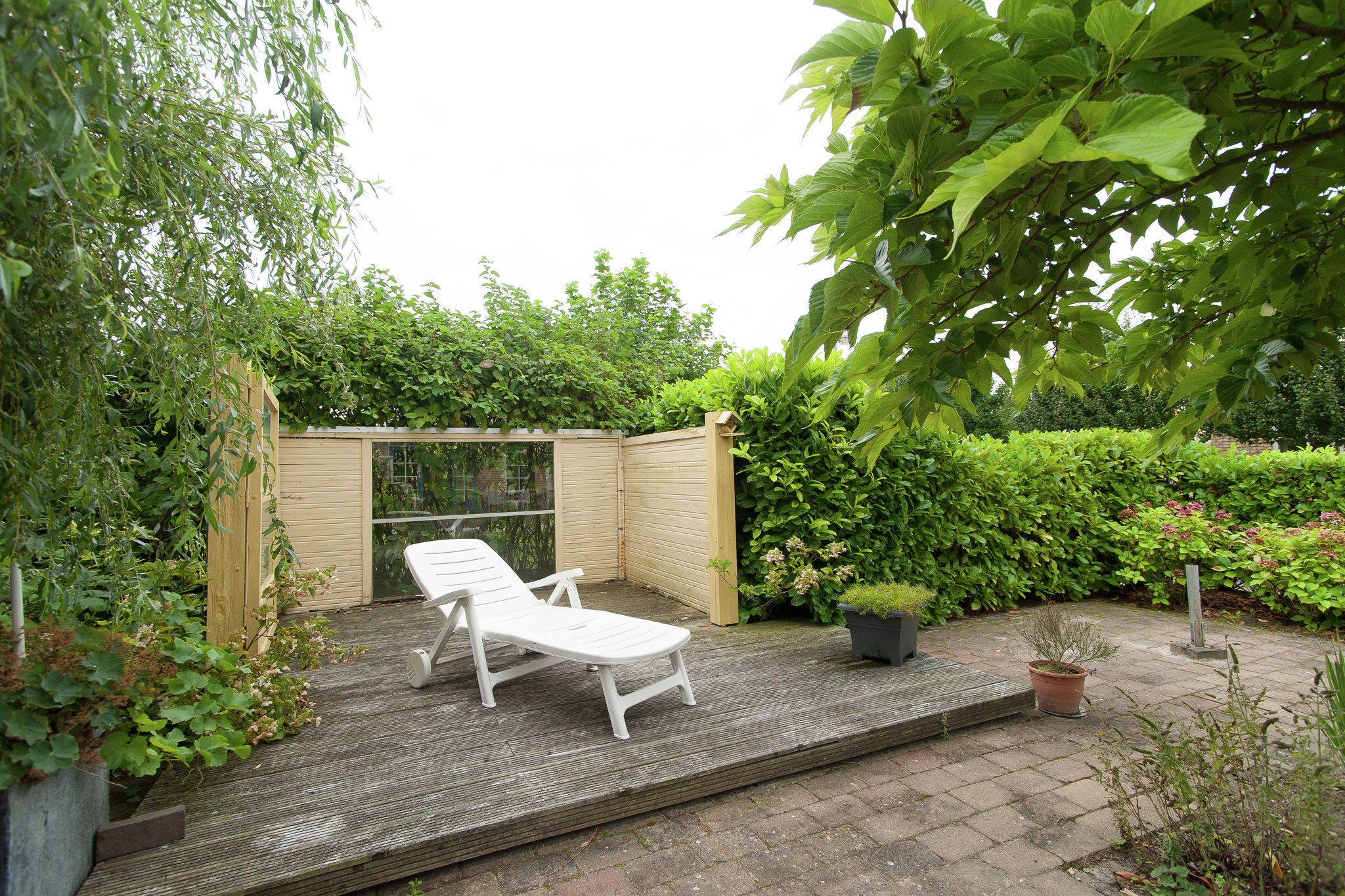 A wooden deck with two white lounge chairs, surrounded by lush greenery and a wooden fence.