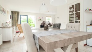 Une cuisine moderne avec une table en bois, des chaises blanches et des luminaires suspendus.