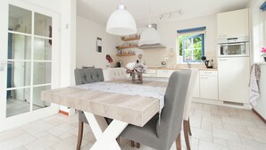 Une cuisine moderne avec des armoires blanches, un four encastré et un coin repas comprenant une table et des chaises en bois.