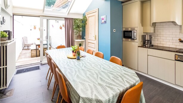 Une cuisine moderne avec un coin repas, comprenant une grande table, des chaises et une vue à travers la porte vitrée.