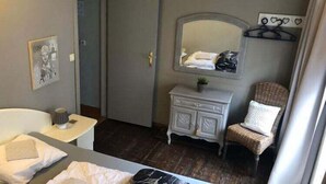 Une chambre d’hôtel avec un lit, une commode, une chaise, un miroir et une porte.