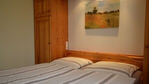A bedroom with a wooden headboard, a bed with striped bedding, and a painting of a field with deer on the wall. - Comfy Apartment in Gransdorf with Garden (Gransdorf)