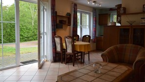 A dining area with a table and chairs, a sofa, and a kitchen area with cabinets and a window. - Comfy Apartment in Gransdorf with Garden (Gransdorf)