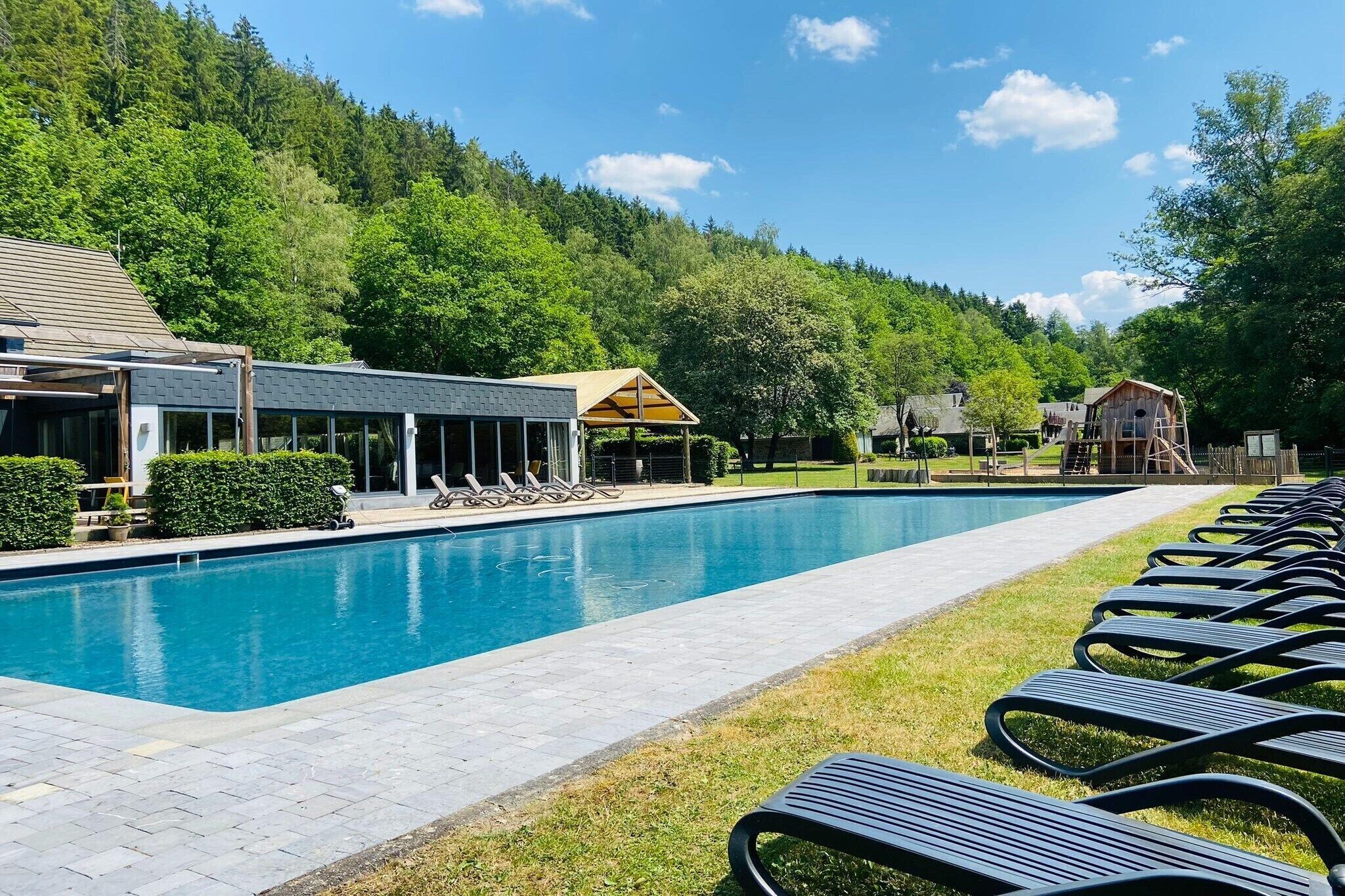 Una piscina con sillas de descanso, un área de estar cubierta y un edificio con techo inclinado.