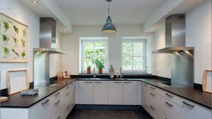 A modern kitchen with white cabinets, black countertops, and a central island. There are two windows providing natural light, and a hanging light fixture above. - Pet-Friendly Mansion (Swolgen)
