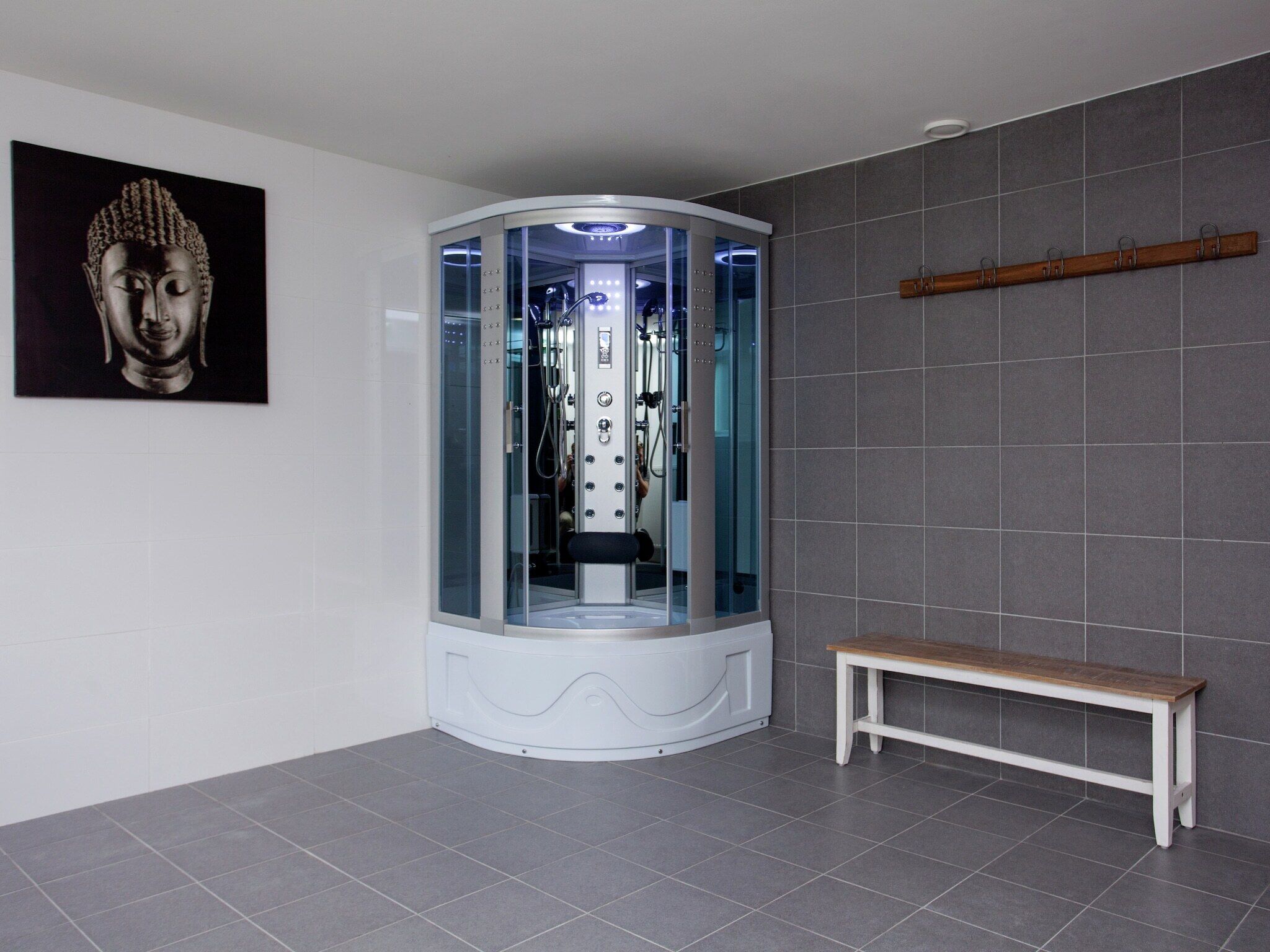 A modern bathroom with a glass-enclosed shower, a wooden bench, and a Buddha statue on the wall.