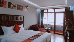 A hotel room with a large bed, a sofa, a small table, and a balcony with a view.