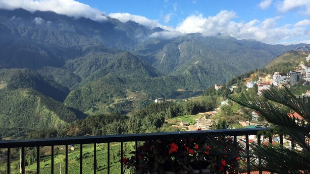 A mountainous landscape with a clear sky, lush greenery, and a few buildings in the distance.