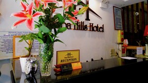 A reception desk at Sapa Hills Hotel with a floral arrangement, a clock, and a sign indicating the reception area.