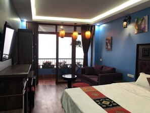 Habitación de hotel con cama, sofá, una mesita y televisor. Tiene un balcón con vistas al exterior.