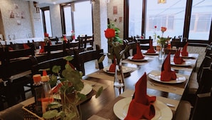 A restaurant with wooden tables set for dining, red napkins, and a vase with a rose.