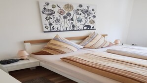 A neatly arranged bedroom with a bed, pillows, a bedside table with a lamp, and a wall-mounted artwork.
