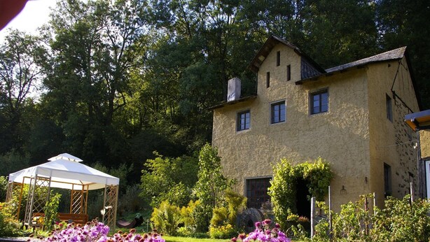 A two-story house with a garden in front, a white gazebo, and a variety of flowers.