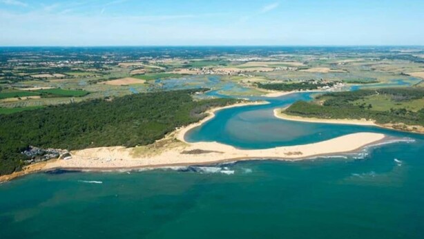 Luchtbeeld van een kustlandschap met een groot waterlichaam, zandstranden en groene gebieden.