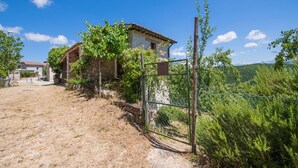 Una casa de piedra rústica con tejado de baldosas, rodeada de vegetación y un cielo azul despejado.