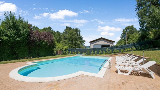 Una piscina con borde curvo, rodeada por un solárium de ladrillo. Hay sillones de descanso a lo largo de la piscina.
