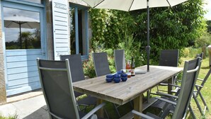 Ein Essbereich im Freien mit einem Holztisch, Metallstühlen, einem Sonnenschirm und einer Flasche BiSoya Wein.