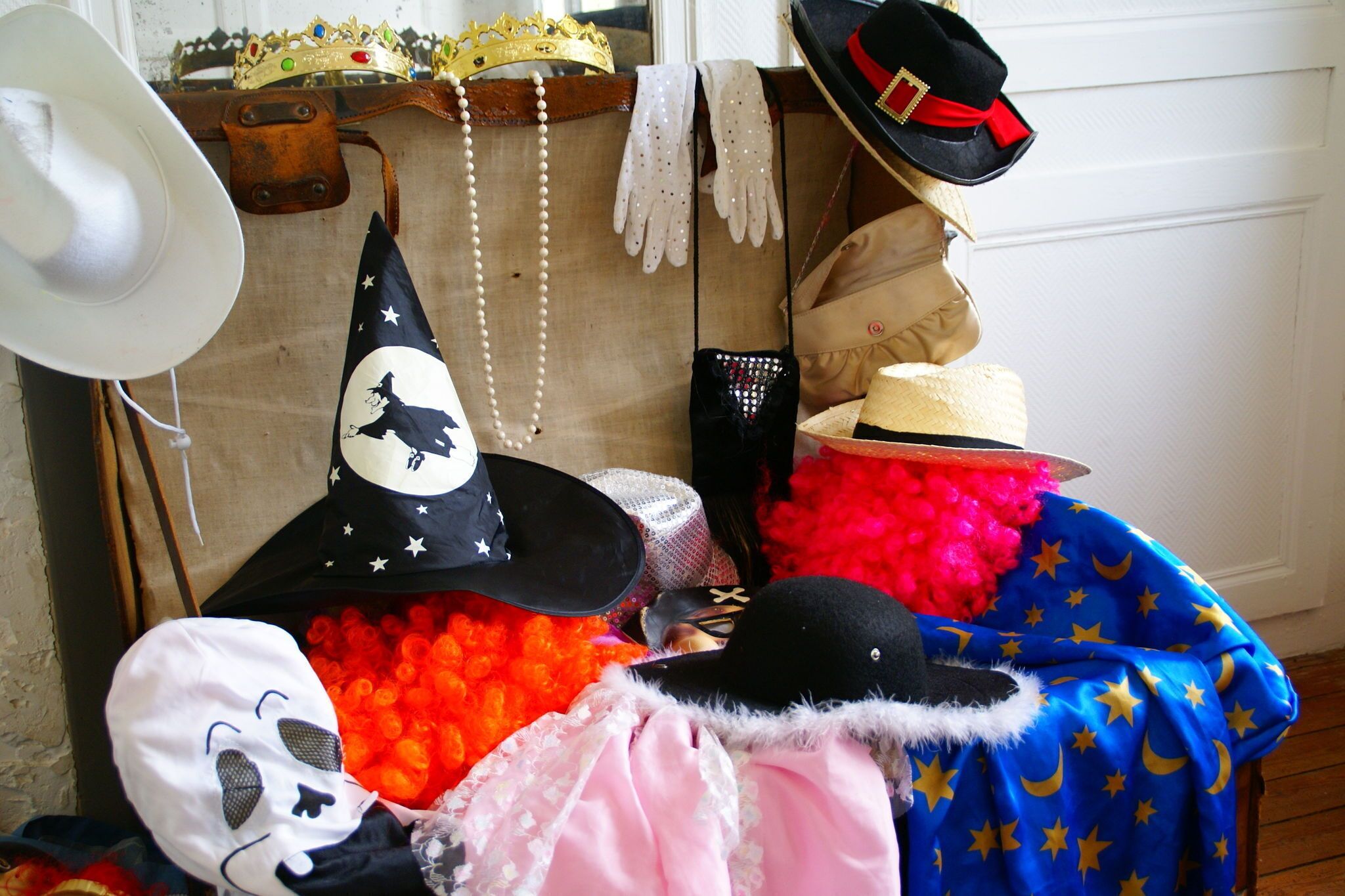 Una colección de sombreros y accesorios, incluyendo un sombrero vaquero blanco, un sombrero de bruja negro y un sombrero negro con una cinta roja.