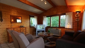 Ein gemütliches Blockhaus-Interieur mit Holzwänden, einem Fernseher, einer Couch und einem Esstisch.