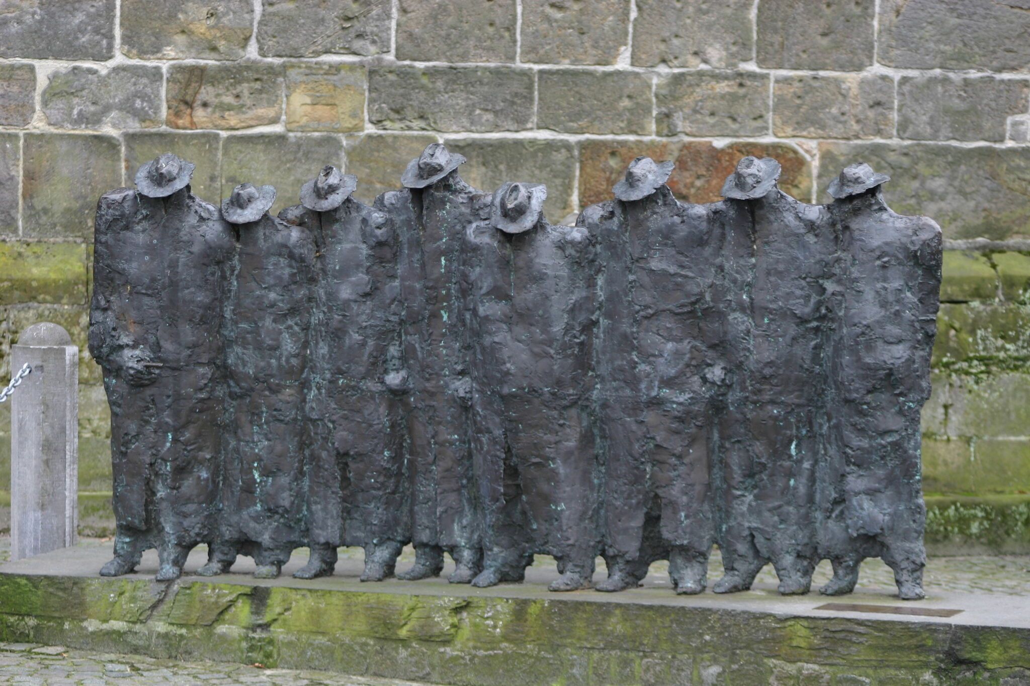Uma fileira de estátuas com chapéus, em frente a uma parede de pedra.