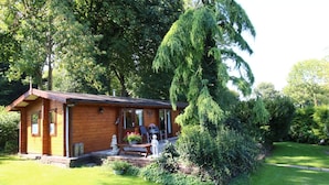Eine Holzhütte mit Veranda, umgeben von üppiger Vegetation und Bäumen.