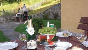 Un tavolo da pranzo all'aperto con una bottiglia di vino Michel, un piatto di uva, fette di anguria e pane.