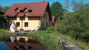 Una casa dal tetto rosso, con un piccolo stagno antistante e un giardino ricco di piante.
