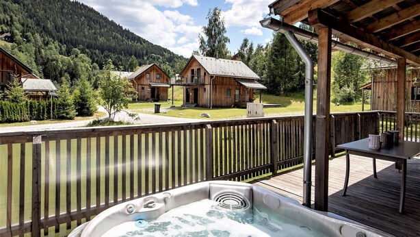 A hot tub on a wooden deck with a view of cabins and mountains.