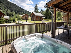 Un bain à remous sur une terrasse en bois, avec vue sur des chalets et des montagnes.