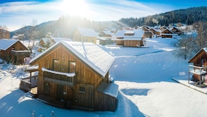 A snow-covered village with wooden cabins, a clear sky, and a bright sun.