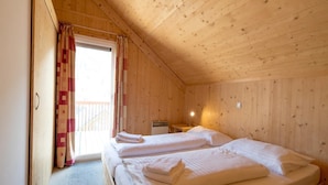 A cozy wooden cabin room with two beds, a small table, and a window with curtains.